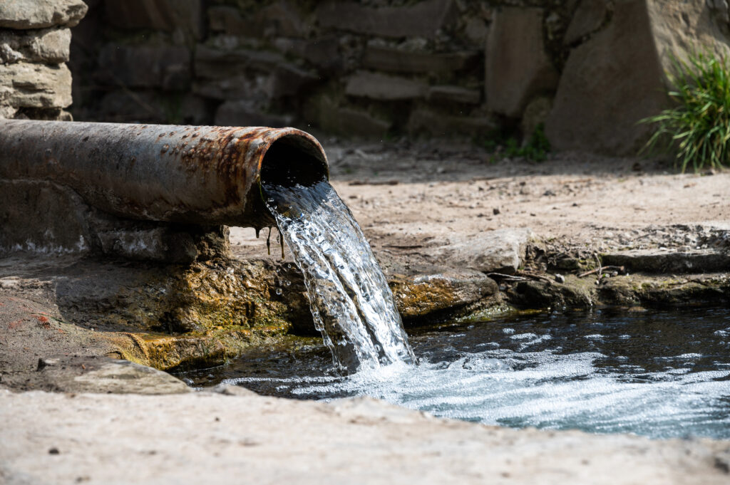 Rohrreinigung - frisches, klares, sauberes Wasser fließt aus einem alten Rohr in einen Bach